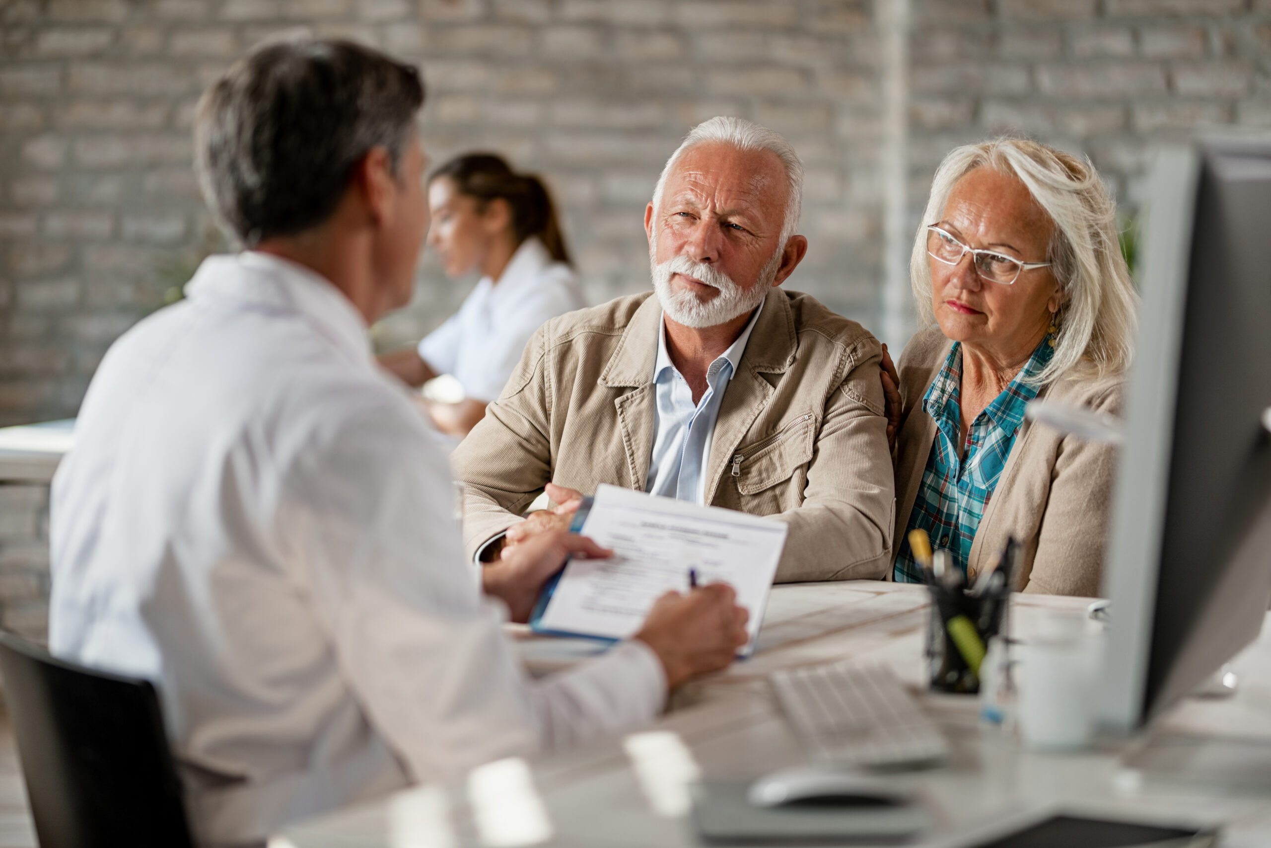 senior couple consulting with healthcare worker about their insurance policy while having meeting clinic scaled